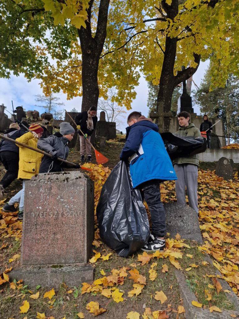 Uczniowie zespołowo sprzątają groby. Źródło: https://www.slovackio.vilniausr.lm.lt/?p=30714&fbclid=IwY2xjawGUZ09leHRuA2FlbQIxMAABHQScwFI0-irxQRJSznrRVZeGZI_KqErOW1jK0Ot1v9gNy8-QIVygTVphXg_aem_-7q63I_FIlMT5O2mdLMKXA&lang=pl